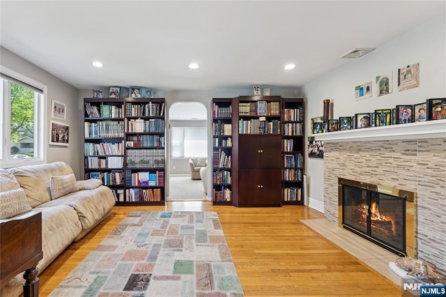 living room featuring arched walkways, a tiled fireplace, recessed lighting, wood finished floors, and visible vents