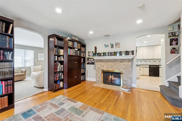 living room with visible vents, a fireplace with flush hearth, arched walkways, wood finished floors, and stairs
