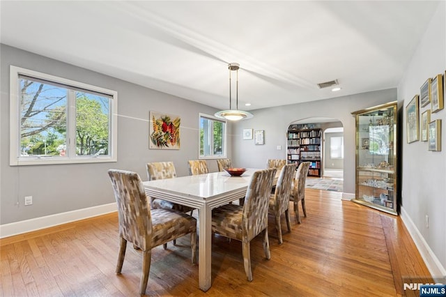 dining area with arched walkways, baseboards, light wood-type flooring, and visible vents