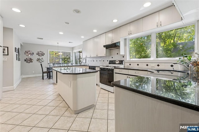 kitchen featuring decorative backsplash, light tile patterned floors, under cabinet range hood, and gas stove