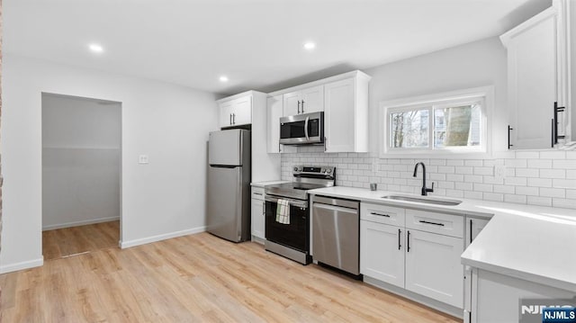 kitchen with stainless steel appliances, a sink, light wood finished floors, and tasteful backsplash