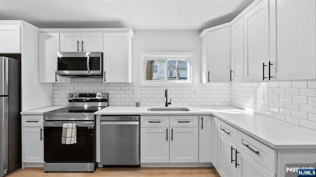 kitchen featuring backsplash, appliances with stainless steel finishes, a sink, light countertops, and white cabinetry