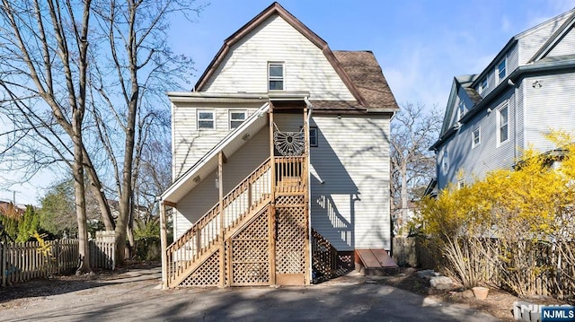 rear view of house with fence, stairs, and a gambrel roof