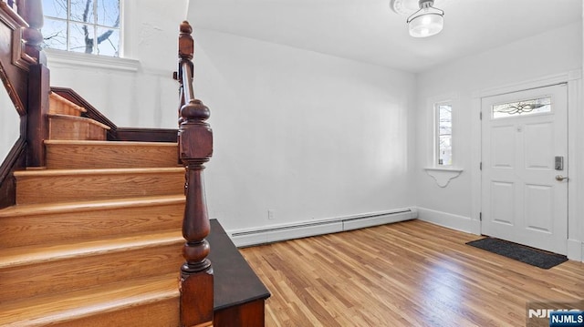 foyer featuring baseboards, a baseboard heating unit, stairs, and wood finished floors