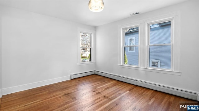 empty room featuring baseboards, visible vents, wood finished floors, and a baseboard radiator