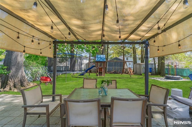 view of patio / terrace with a fenced backyard, a storage unit, a playground, a trampoline, and an outbuilding