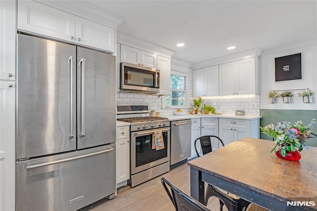 kitchen with crown molding, appliances with stainless steel finishes, light countertops, white cabinetry, and backsplash