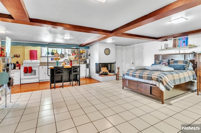 bedroom with a brick fireplace, light tile patterned flooring, and beamed ceiling
