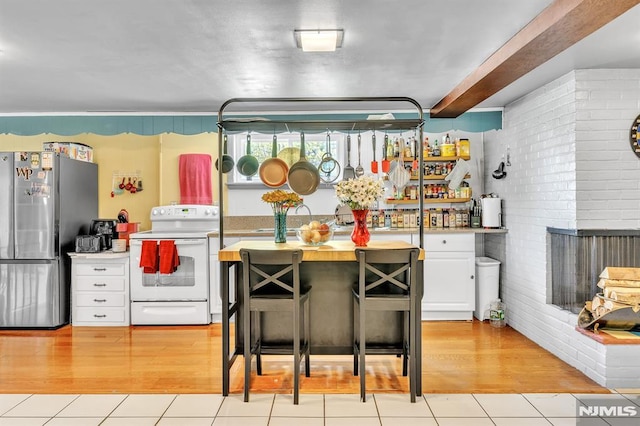 kitchen featuring white cabinets, electric range, brick wall, freestanding refrigerator, and light tile patterned floors