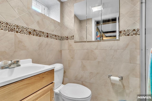 half bath with toilet, tile walls, and vanity