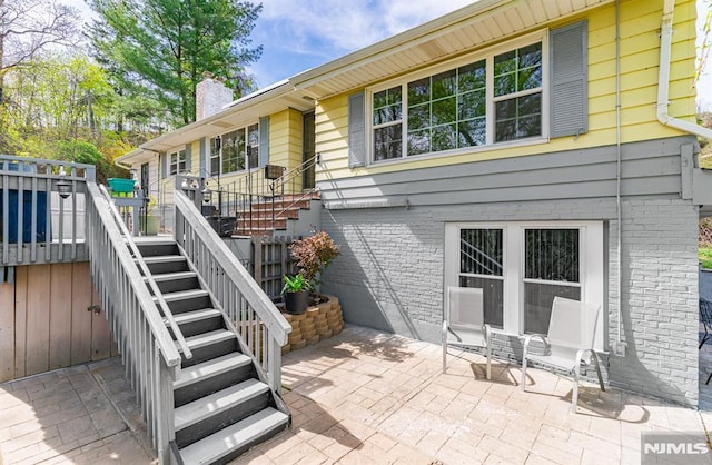 back of house with a chimney, a wooden deck, a patio area, stairway, and brick siding