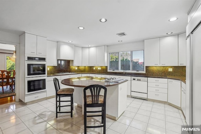 kitchen with a sink, dark countertops, white cabinets, and white appliances