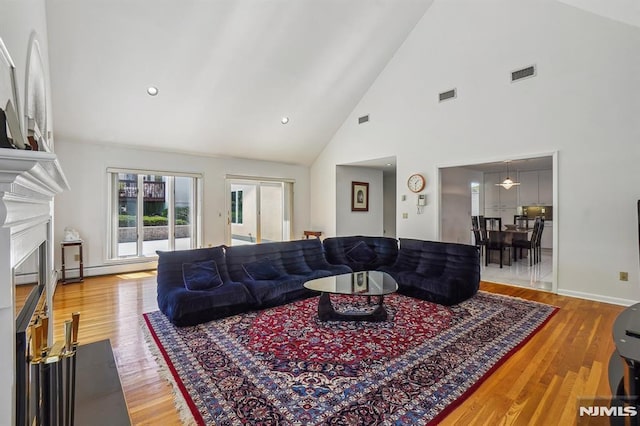 living room featuring high vaulted ceiling, visible vents, a fireplace with flush hearth, and wood finished floors