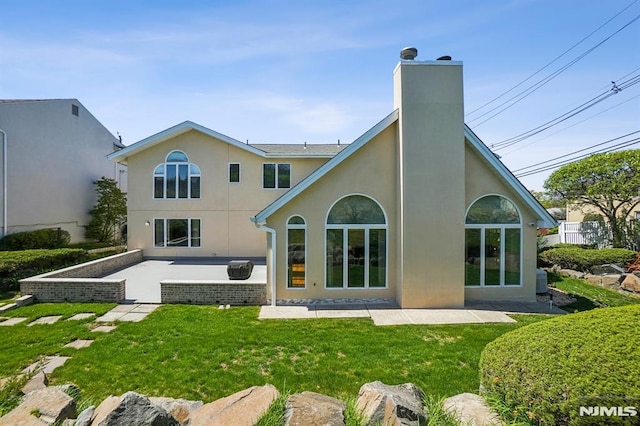 back of property featuring a lawn, a patio, a chimney, and stucco siding