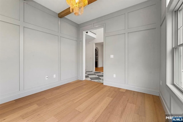 229 Bogert Pl, Paramus, NJ 07652 - unfurnished bedroom featuring arched walkways, beam ceiling, light wood finished floors, a notable chandelier, and a decorative wall