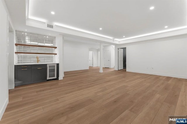 229 Bogert Pl, Paramus, NJ 07652 - unfurnished living room with visible vents, indoor wet bar, beverage cooler, a tray ceiling, and light wood-style flooring