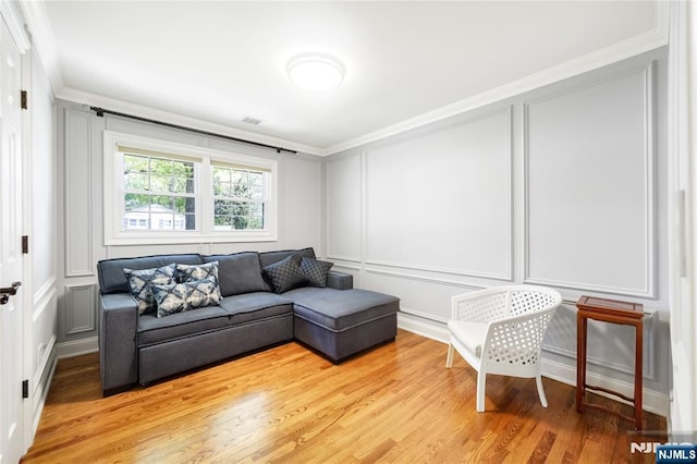 living area featuring crown molding, light wood-style flooring, a decorative wall, and visible vents