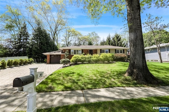 single story home featuring driveway, a garage, brick siding, fence, and a front lawn