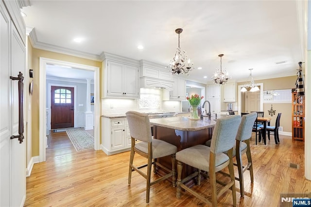 dining space featuring an inviting chandelier, ornamental molding, and light wood-style floors