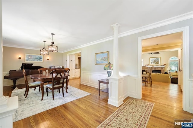 dining space featuring light wood-style floors, ornamental molding, decorative columns, and a wainscoted wall