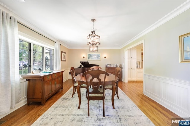 dining space with a chandelier, ornamental molding, light wood finished floors, and a wainscoted wall