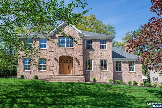 colonial inspired home featuring brick siding, a shingled roof, and a front yard