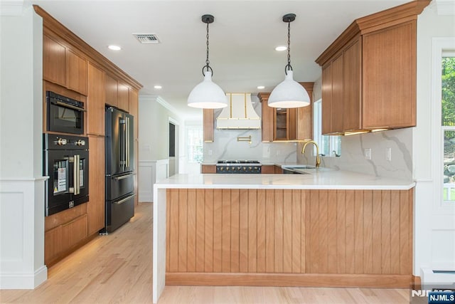 kitchen featuring visible vents, a peninsula, wall chimney range hood, a sink, and black appliances