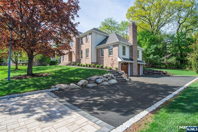 view of front of house with an attached garage, brick siding, a front yard, a chimney, and driveway