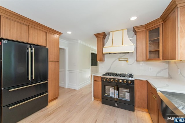kitchen with brown cabinetry, crown molding, wainscoting, premium range hood, and black appliances