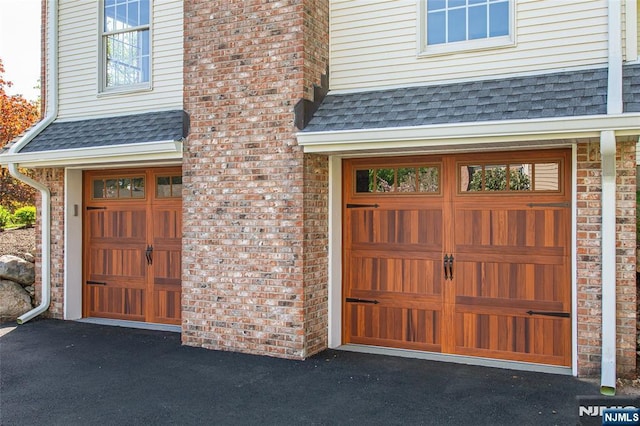 doorway to property featuring an attached garage, driveway, a chimney, and roof with shingles