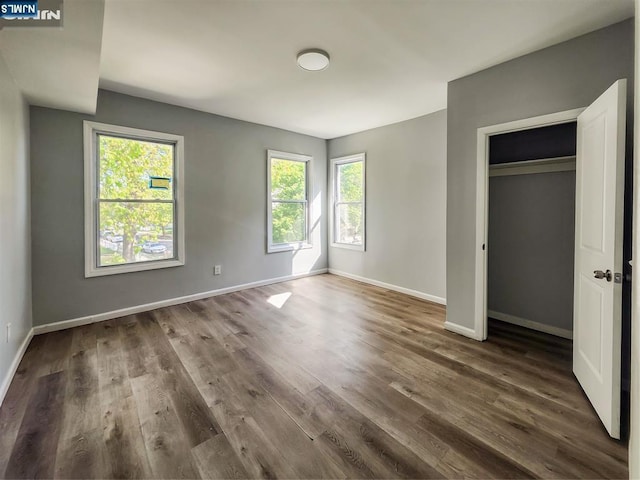 unfurnished bedroom featuring baseboards, multiple windows, and wood finished floors