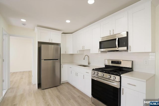 kitchen with light countertops, white cabinetry, a sink, backsplash, and stainless steel appliances