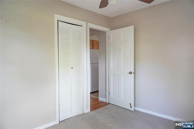 unfurnished bedroom featuring a closet, freestanding refrigerator, baseboards, ceiling fan, and carpet flooring
