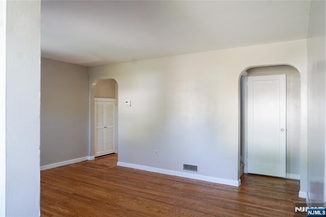unfurnished room with visible vents, arched walkways, baseboards, and wood finished floors