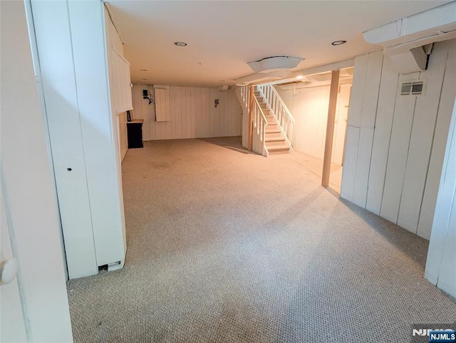 finished basement featuring stairway, visible vents, wood walls, and carpet