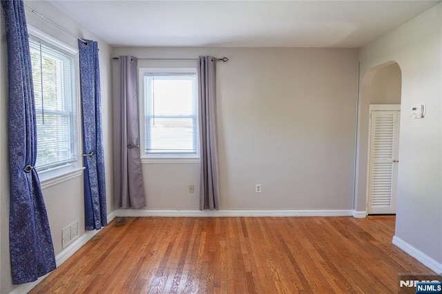 spare room featuring arched walkways, baseboards, visible vents, and wood finished floors