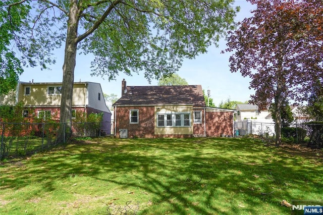 rear view of house with a lawn, brick siding, a chimney, and a fenced backyard