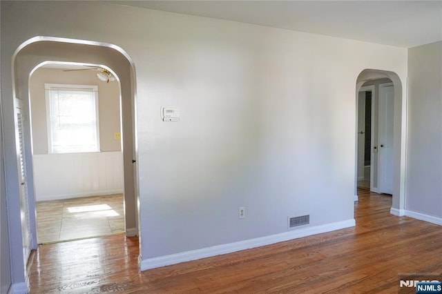 empty room featuring arched walkways, baseboards, visible vents, and wood finished floors
