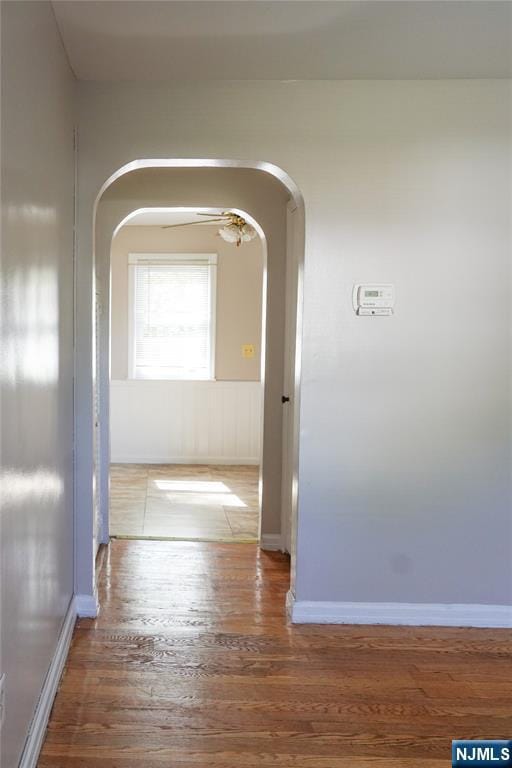 hall featuring baseboards, arched walkways, and wood finished floors
