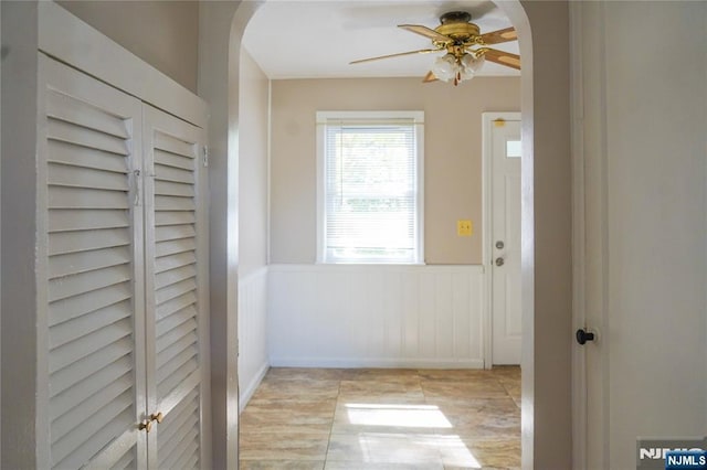 interior space with arched walkways, ceiling fan, and a wainscoted wall