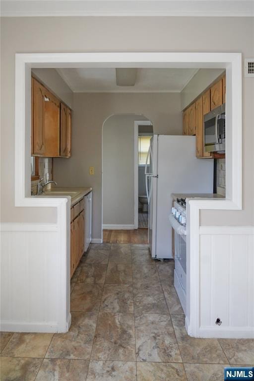 kitchen featuring a sink, white appliances, arched walkways, light countertops, and brown cabinetry