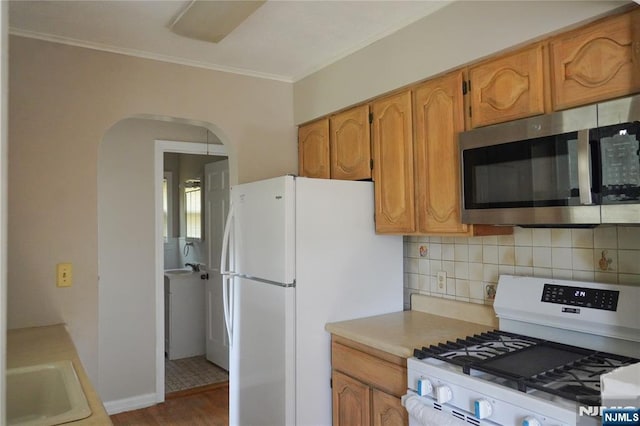 kitchen with arched walkways, tasteful backsplash, a sink, ornamental molding, and white appliances
