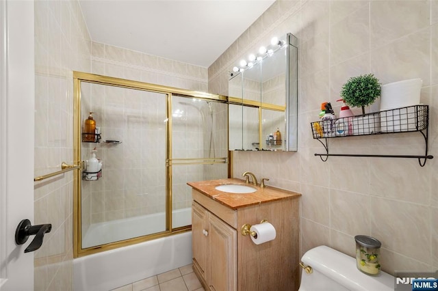 bathroom featuring shower / bath combination with glass door, vanity, toilet, tile patterned floors, and tile walls