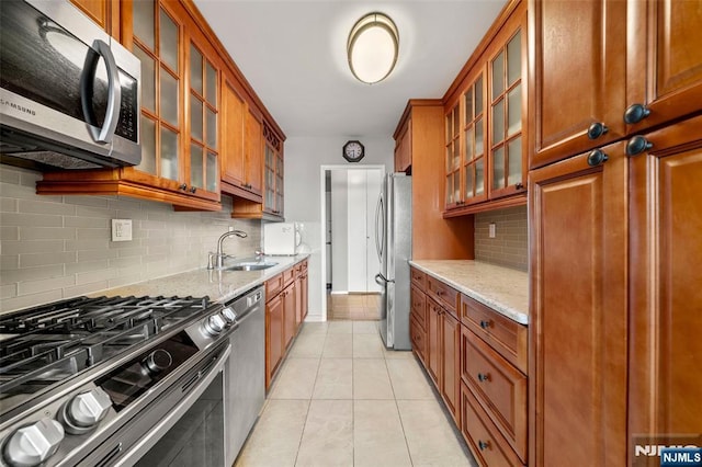 kitchen featuring a sink, appliances with stainless steel finishes, light stone counters, and glass insert cabinets