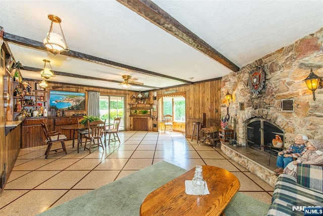 living area featuring a fireplace, beamed ceiling, wooden walls, a textured ceiling, and a ceiling fan