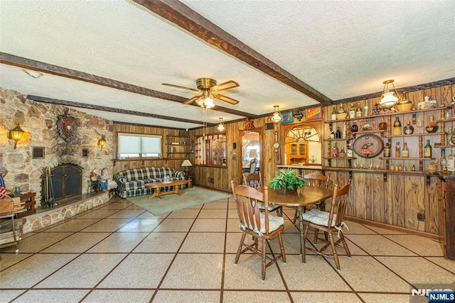dining space with beam ceiling, a stone fireplace, wood walls, and a textured ceiling