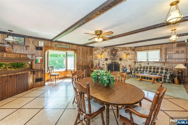 dining space with a healthy amount of sunlight, beam ceiling, wood walls, and a textured ceiling