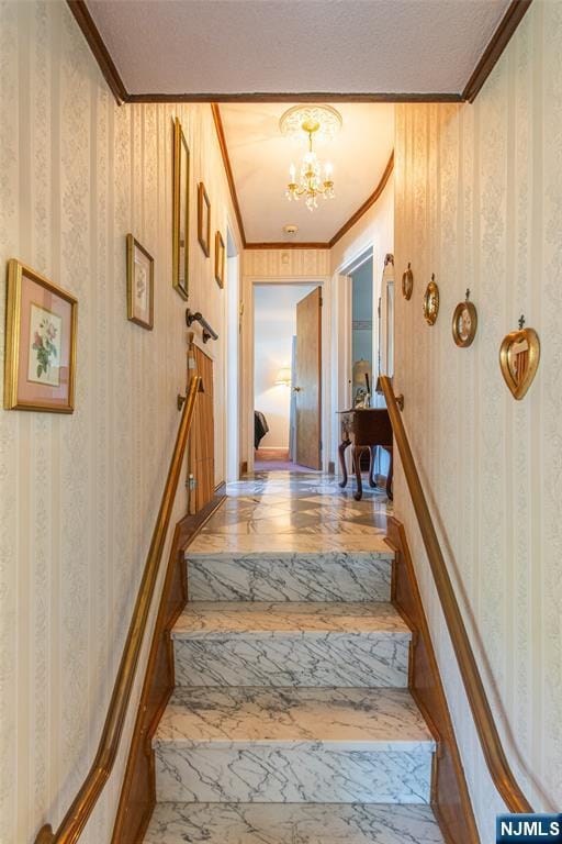 stairway featuring crown molding, a textured ceiling, a notable chandelier, and wallpapered walls