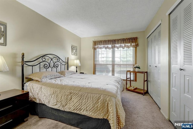 carpeted bedroom featuring a textured ceiling and multiple closets