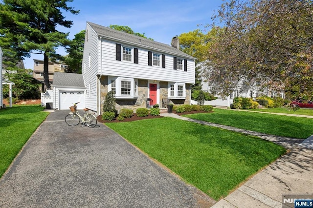 colonial house with stone siding, a chimney, a front yard, and aphalt driveway